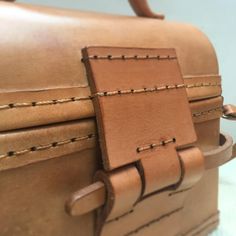 a brown leather suitcase with stitching on the handle and strap around it's corners