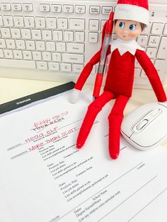 an elf with a pen sitting on top of a sheet of paper next to a computer keyboard