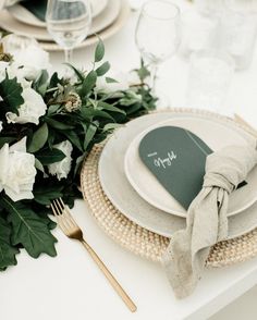 a place setting with white flowers and greenery