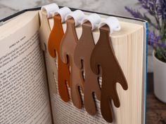 an open book with five different colored wooden hands on it's cover, sitting next to a purple flower