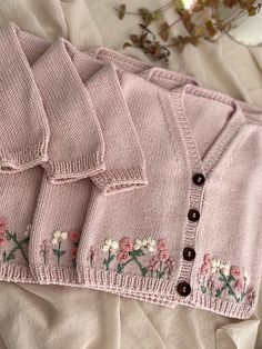 three pink sweaters with flowers and buttons on them