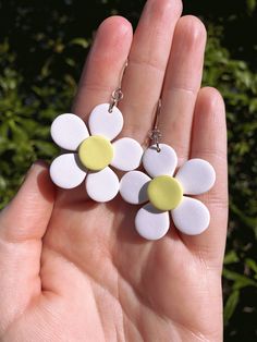 two white and yellow flower earrings are held in someone's hand