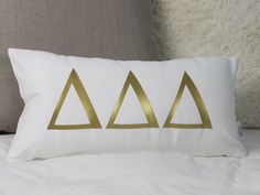 a white pillow with three gold triangles on the front and back, sitting on top of a bed