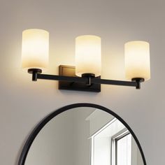 a bathroom vanity light with three lights on the side and a round mirror above it