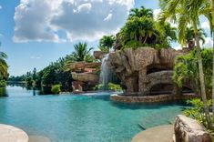 an outdoor pool with waterfall and slide in the middle, surrounded by palm trees on either side