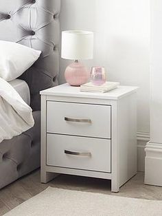 a white nightstand with two drawers and a pink lamp on the end table next to it