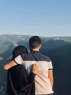 a man and woman standing on top of a mountain looking at the mountains in the distance