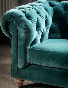 a green velvet couch sitting on top of a wooden floor