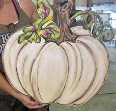 a woman holding a large white pumpkin painted with acrylic paint on it's side