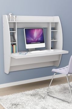 a desk with a computer on it and a chair next to it in front of a blue wall