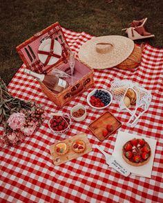 a picnic with straw hats, fruit and bread on a checkered tablecloth in the grass