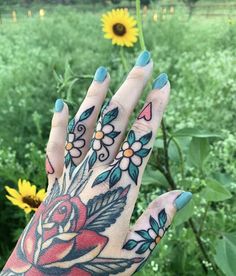 a woman's hand with tattoos on it in front of flowers and sunflowers