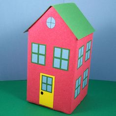 a paper doll house with a green roof and yellow door on a green table top