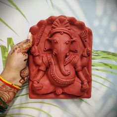 a hand is holding an intricately carved ganeshi idol, with palm leaves in the background