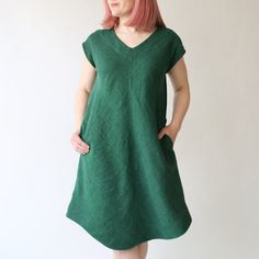 a woman standing in front of a white wall wearing a green dress and pink hair