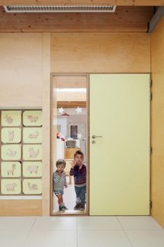 two children standing in the doorway of a room with wooden walls and white tile flooring