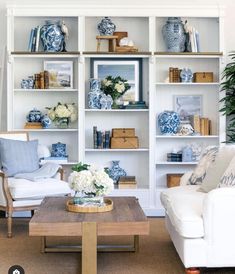 a living room filled with white furniture and blue and white decor on the shelves above