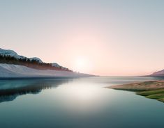 the sun is setting over a lake with snow on the mountains and grass in the foreground