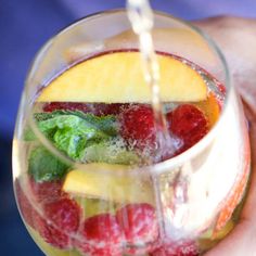 a person holding a wine glass filled with fruit and water pouring out of the top