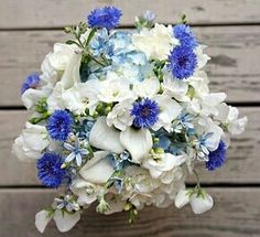 a bridal bouquet with blue and white flowers in front of wooden planks on the wall