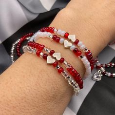 two bracelets with red and white beads on the wrist, one has silver heart charms