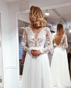 a woman in a wedding dress looking at herself in the mirror with her back to the camera