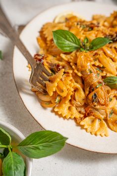 a white plate topped with pasta covered in sauce and basil leaves next to a fork