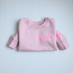 This Barbie Crew Sweater is sure to keep your child warm and cozy during the colder months. Its snug material is comfortable and lightweight, and its light pink color adds a cheerful touch. Perfect for any Barbie fan! * Glow in the dark Hot Pink Barbie font and silhouette. Pink Crew Neck Sweater In Acrylic, Pink Crew Neck Acrylic Sweater, Pink Crew Neck Sweater With Text Print, Barbie Crewneck, Playful Pink Crew Neck Sweater, Light Pink Color, Girls Sweaters, Barbie Girl, Warm And Cozy