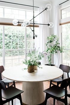 a dining room table with chairs and a potted plant on it in front of large windows