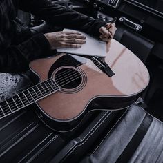 a person sitting in a car holding a guitar and writing on a piece of paper