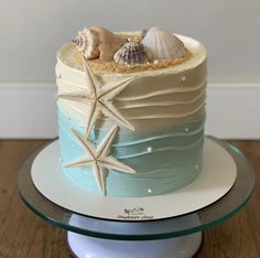 a blue and white cake with sea shells on the top is sitting on a plate