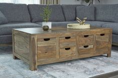 a wooden coffee table with drawers on it in front of a gray couch and rug