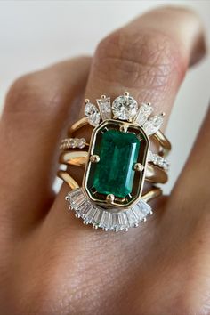 a woman's hand holding an emerald and diamond ring