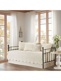 a white day bed sitting in front of two windows next to a vase with flowers