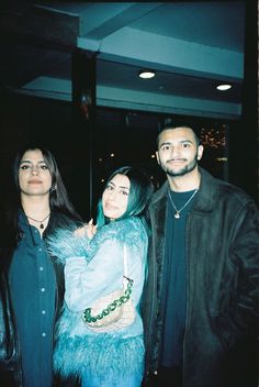 three people standing next to each other in front of a building and one person is wearing a fur coat