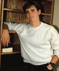 a young man leaning against a book shelf with his hand on the top of it