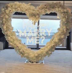 a heart - shaped flower arrangement with the words will you marry me? in front of a window