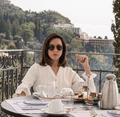 a woman sitting at a table with food and drinks in front of her on the balcony