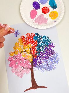 a paper plate with an image of a tree painted on it and a hand holding a crayon pencil