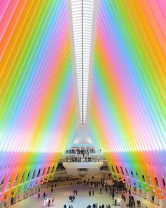 the inside of a building with many people walking around and rainbow colored lines on the ceiling