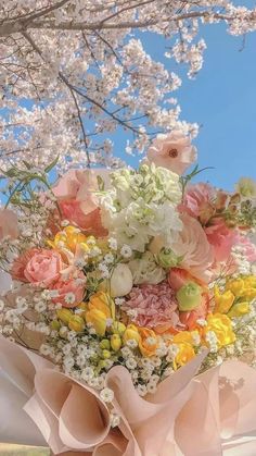 a bunch of flowers that are sitting in the grass near some trees with white and pink flowers