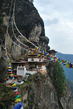 many colorful flags are hanging from the side of a mountain with a building on top