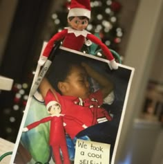 an elf is sitting on top of a shelf next to a christmas tree and a sign that says we took a cool selfie snowy