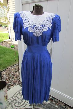 Vintage blue Karin Stevens dress in size 6 petite.  Apparently has never been worn; all the original tags are still on.  Back buttons from top to waist and then a zipper from the waist down.  Of course it has shoulder pads!  But they can easily be removed.  Elbow length sleeves gathered at the shoulder.  A stunning piece of lace is attached at the front.  Fitted elasticized/shirred waist in the back.  And the cutest little pockets at the front sides.  100% rayon. There are two faint whitish line Retro Blue Puff Sleeve Dress, Fitted Blue Vintage Dress With Lace Trim, Blue Peter Pan Collar Dress For Daywear, Blue Retro Dress With Peter Pan Collar, Yarn Tote Bag, Cornflower Blue, Puffed Sleeves, Elbow Length Sleeve, Lace Applique