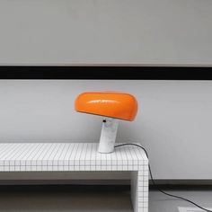 an orange chair sitting on top of a white bench in front of a wall and window