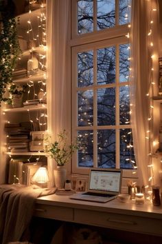 a laptop computer sitting on top of a desk under a window covered in fairy lights