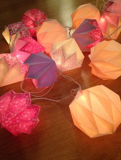 several paper umbrellas sitting on top of a wooden table with string lights attached to them