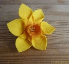 a small yellow flower sitting on top of a wooden table next to a piece of wood