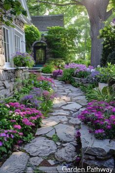 a stone path is surrounded by colorful flowers and greenery in front of a house