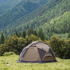 a tent pitched up in the grass with mountains in the background